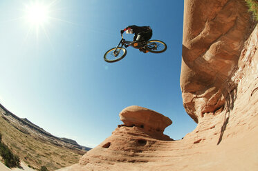 Low angle view of mountain biker jumping from cliff against clear blue sky - CAVF06208