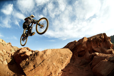 Cyclist jumping from rocks against cloudy sky - CAVF06217