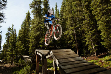 Low angle view of man performing stunt on sports ramp in forest - CAVF06225