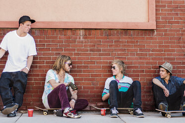 Freunde mit Skateboard im Gespräch, während sie an einer Mauer sitzen - CAVF06252