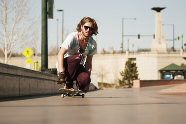 Mann mit Sonnenbrille fährt auf dem Gehweg Skateboard - CAVF06255