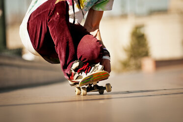 Niedriger Ausschnitt eines Mannes, der sich beim Skateboardfahren auf dem Gehweg duckt - CAVF06256