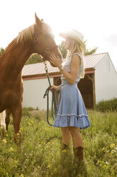 Seitenansicht eines Cowgirls, das ein Pferd streichelt, während es auf einem Feld steht - CAVF06276
