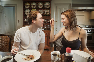 Woman feeding man while sitting at dining table in home - CAVF06326