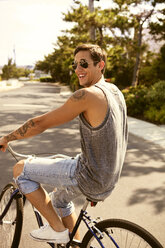 Seitenansicht eines glücklichen Mannes beim Fahrradfahren auf der Straße - CAVF06423