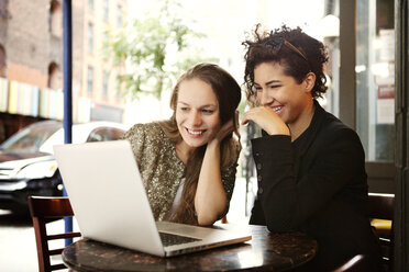 Freunde benutzen einen Laptop, während sie in einem Straßencafé sitzen - CAVF06438