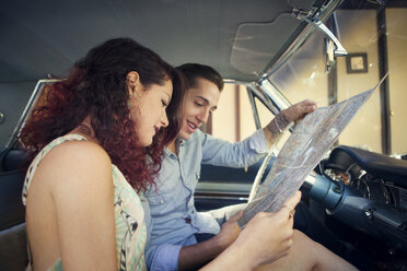 Couple looking at map while sitting in vintage car - CAVF06444