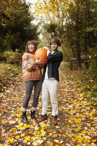 Porträt eines Paares, das einen Halloween-Kürbis trägt und auf einem Feld steht, lizenzfreies Stockfoto