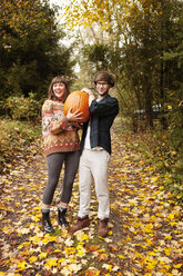 Porträt eines Paares, das einen Halloween-Kürbis trägt und auf einem Feld steht - CAVF06459