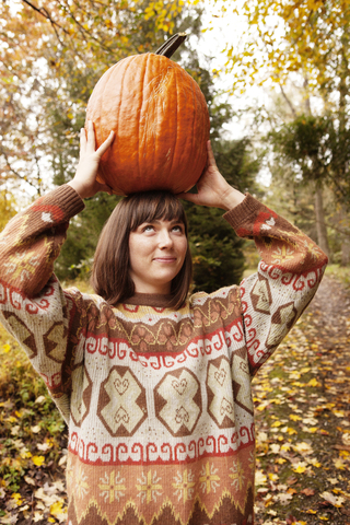 Frau schaut nach oben, während sie einen Halloween-Kürbis trägt, lizenzfreies Stockfoto