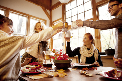 Freunde stoßen feierlich am Tisch im Haus an, lizenzfreies Stockfoto