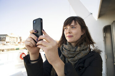 Frau, die während der Fahrt in einem Passagierflugzeug mit ihrem Mobiltelefon fotografiert - CAVF06484