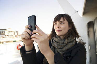 Woman photographing through mobile phone while traveling in passenger craft - CAVF06484