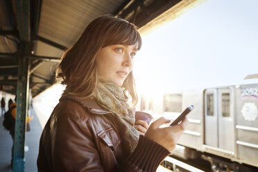 Frau schaut weg, während sie am Bahnhof ihr Smartphone benutzt - CAVF06492