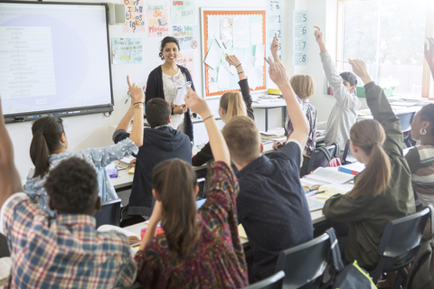 Rear view of teenage students raising hands in classroom stock photo