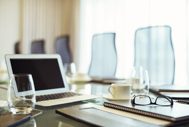 Laptop, eyeglasses and diary on conference table in empty conference room - CAIF15245