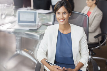 Portrait of smiling businesswoman posing with tablet pc in conference room - CAIF15250