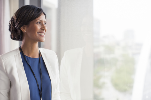 Porträt einer lächelnden erwachsenen Frau, die durch ein Fenster schaut, lizenzfreies Stockfoto