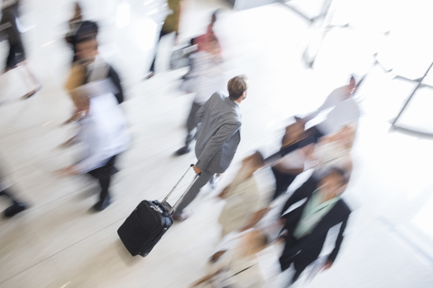 Geschäftsmann geht durch die Lobby eines öffentlichen Gebäudes in Richtung Ausgang, mit einem Rollkoffer, lizenzfreies Stockfoto