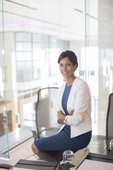 Porträt einer schönen lächelnden Geschäftsfrau, die an einem Glastisch in einem Konferenzraum sitzt - CAIF15278