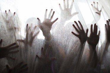Silhouette von Menschen, die hinter einem transparenten Vorhang die Hände heben - CAIF15283