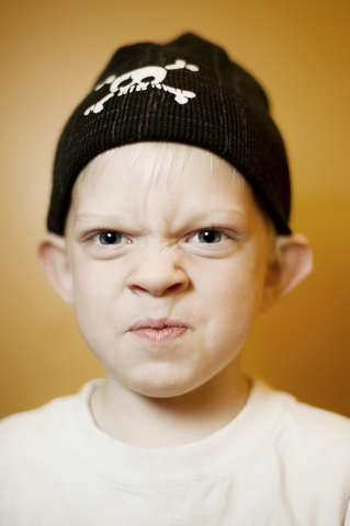 Porträt eines Jungen mit Strickmütze vor orangefarbenem Hintergrund, lizenzfreies Stockfoto