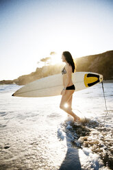 Side view of woman with surfboard walking in water at beach - CAVF06541