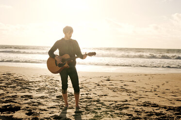 Man playing guitar while standing at beach - CAVF06641