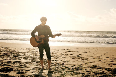 Mann spielt Gitarre am Strand stehend - CAVF06641