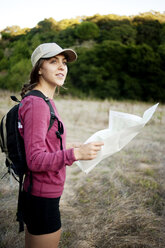 Side view of female hiker holding map while standing on field - CAVF06653