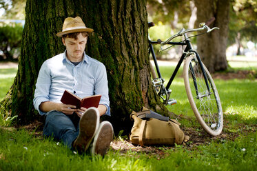 Glücklicher Mann liest ein Buch, während er mit dem Fahrrad im Park sitzt - CAVF06683