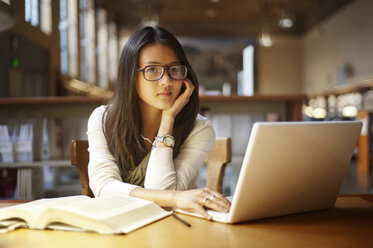 Porträt einer Frau, die einen Laptop benutzt, während sie in einer Bibliothek sitzt - CAVF06721
