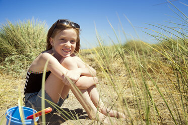 Porträt eines glücklichen Mädchens im Sand sitzend gegen den klaren Himmel - CAVF06732