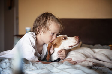 Junge, der seinen Hund umarmt, während er zu Hause auf dem Bett liegt - CAVF06748