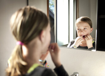 Girl flossing teeth in bathroom seen through mirror - CAVF06780