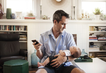 Man using mobile phone while looking at baby boy - CAVF06874