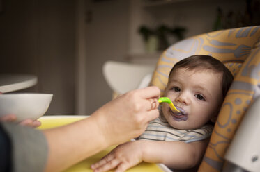 Beschnittenes Bild einer Mutter, die einen kleinen Jungen zu Hause mit der Hand füttert - CAVF06907