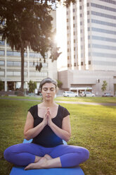 Frau meditiert auf einer Übungsmatte im Park sitzend - CAVF06950