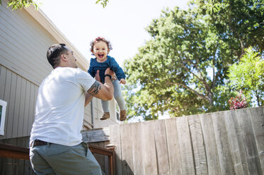 Low angle view of father lifting daughter while standing in backyard - CAVF06956