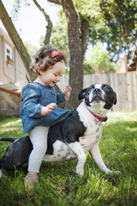 Glückliches kleines Mädchen sitzt auf einem Hund im Hinterhof - CAVF06961