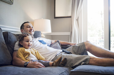 Glücklicher Vater und Tochter entspannen sich auf dem Sofa zu Hause - CAVF06963