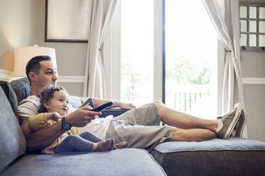 Father and daughter watching television at home - CAVF06964