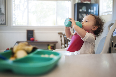 Baby-Mädchen trinkt, während es zu Hause im Hochstuhl sitzt, lizenzfreies Stockfoto