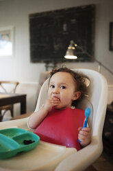 Baby girl eating while sitting in high chair at home - CAVF06969