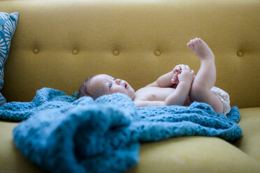 Kleines Baby auf blauem Tuch liegend, mit angehobenen Beinen, einen Fuß haltend - CAIF15325