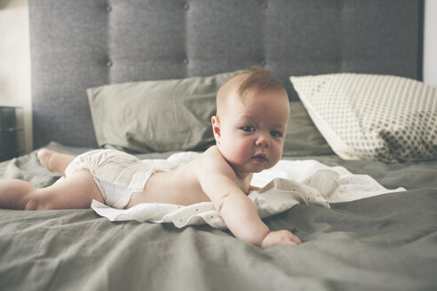 Porträt eines kleinen Babys, das mit erhobenem Kopf auf der Vorderseite eines Bettes liegt - CAIF15335