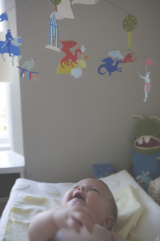 Kleines Baby liegt und betrachtet das bunte hängende Mobile, lizenzfreies Stockfoto
