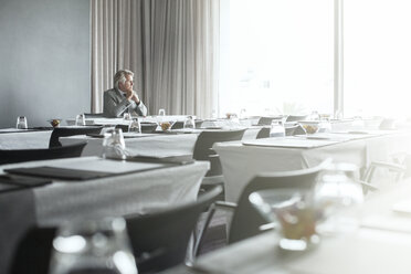 Älterer Geschäftsmann sitzt mit verschränkten Händen in einem Bürorestaurant - CAIF15420