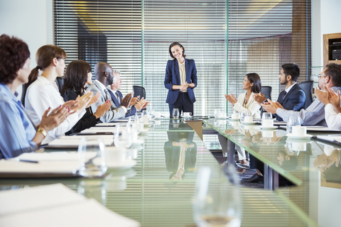 Conference participants applauding to young businesswoman standing at head of conference table stock photo