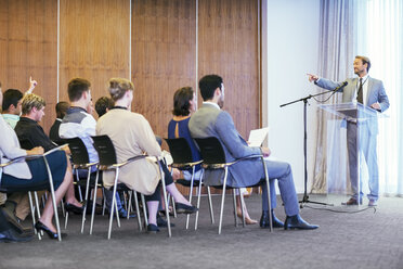 Porträt eines Geschäftsmannes, der an einem transparenten Rednerpult steht und vor einem Publikum in einem Konferenzraum spricht - CAIF15485